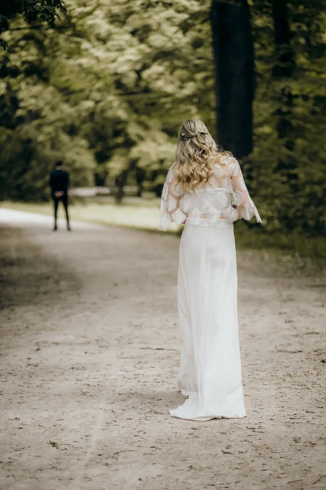 Braut in weißem Kleid mit blonden Locken auf einem Waldweg nach der Trauung in München, fotografiert von MOKATI
