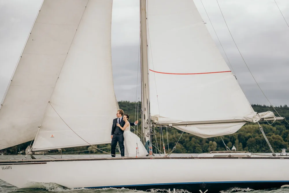 Braut und Bräutigam stehen auf einem Segelboot mit weißen Segeln. Hochzeitsfotograf MOKATI
