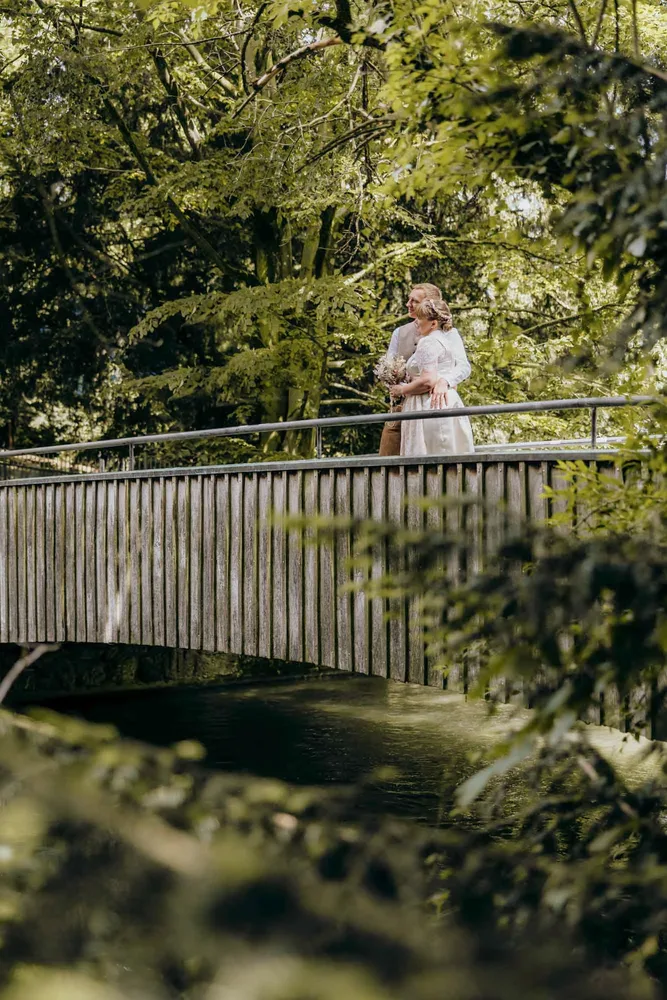 Paar steht lächelnd auf einer Brücke über einem Fluss nach standesamtlicher Trauung in München, fotografiert von MOKATI
