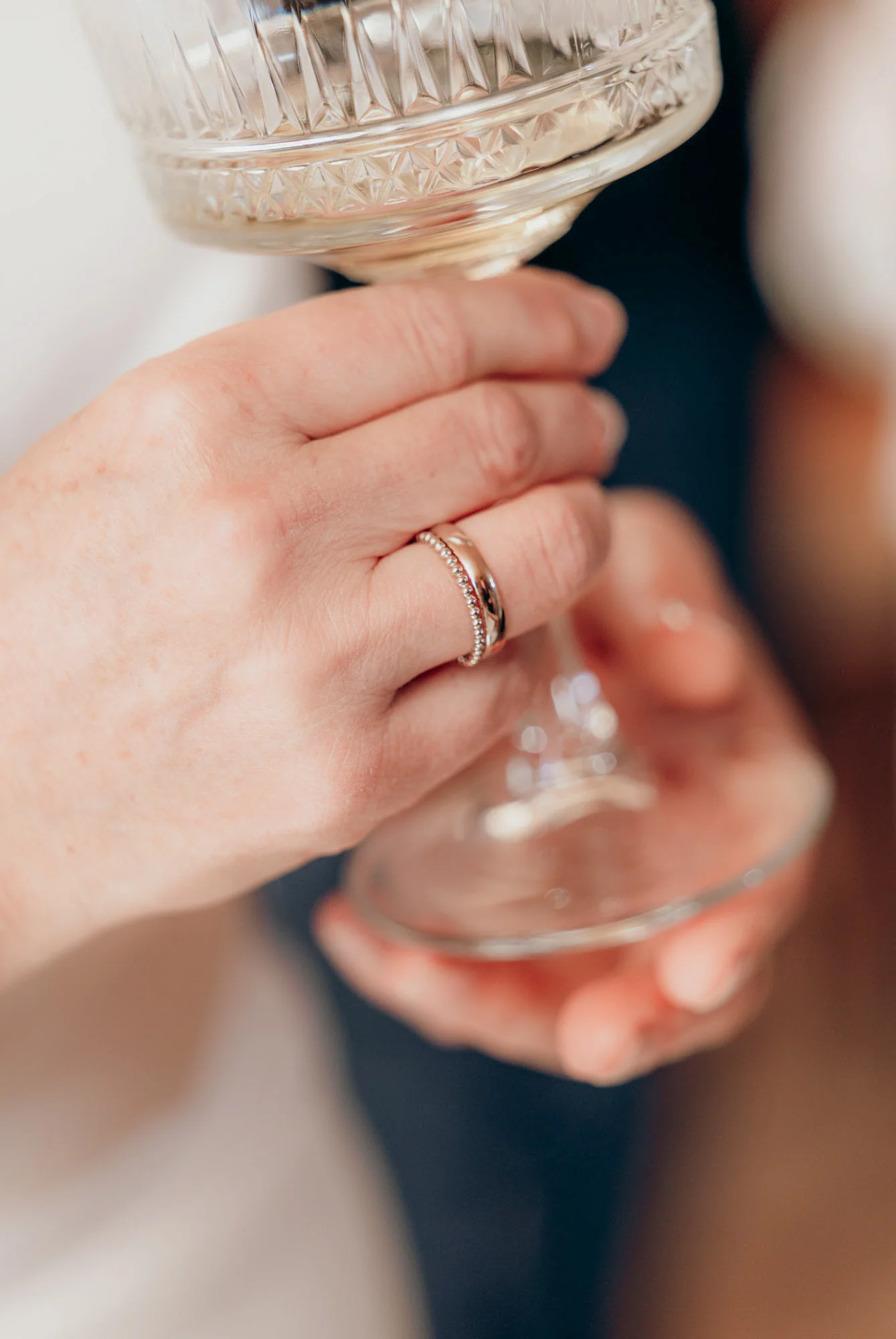 Hand mit zwei Eheringen hält ein Champagnerglas