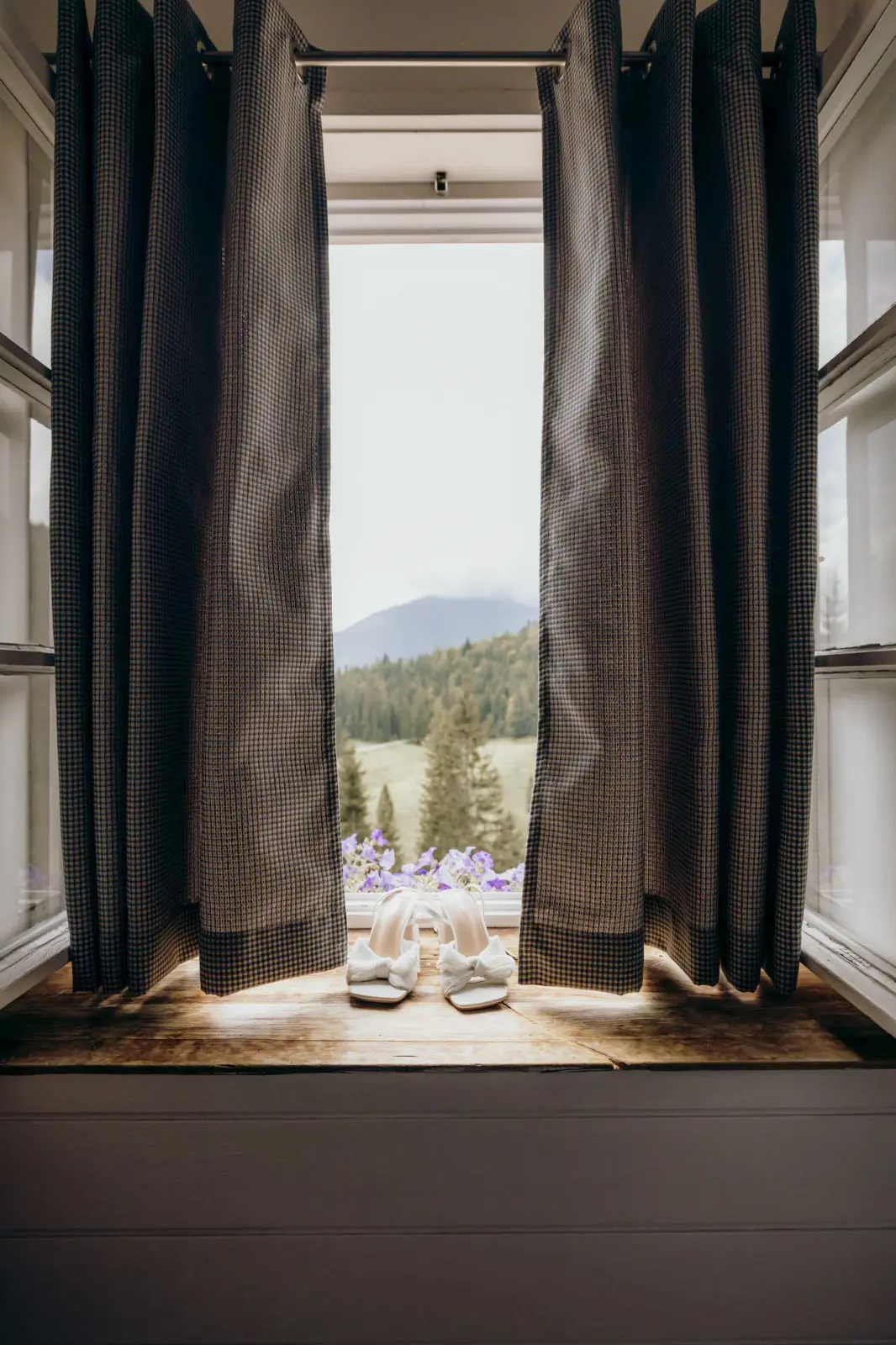 Brautschuhe auf der hölzernen Fensterbank im Almbad Sillberghaus, dahinter Bergwald und Wiese