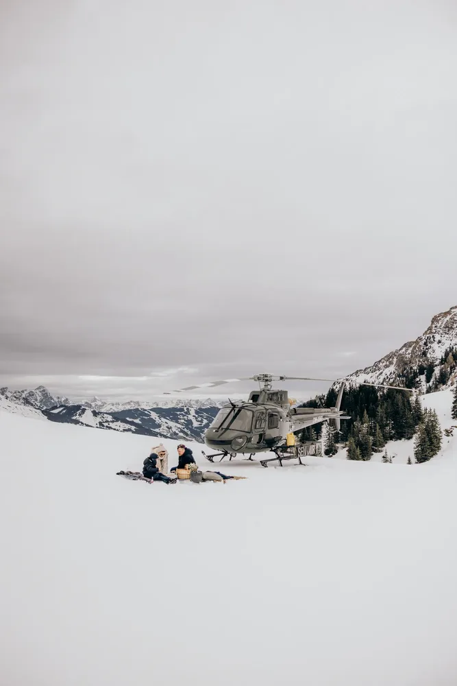 Zwei Personen sitzen im Schnee neben einem Helikopter. Hochzeitsfotograf MOKATI