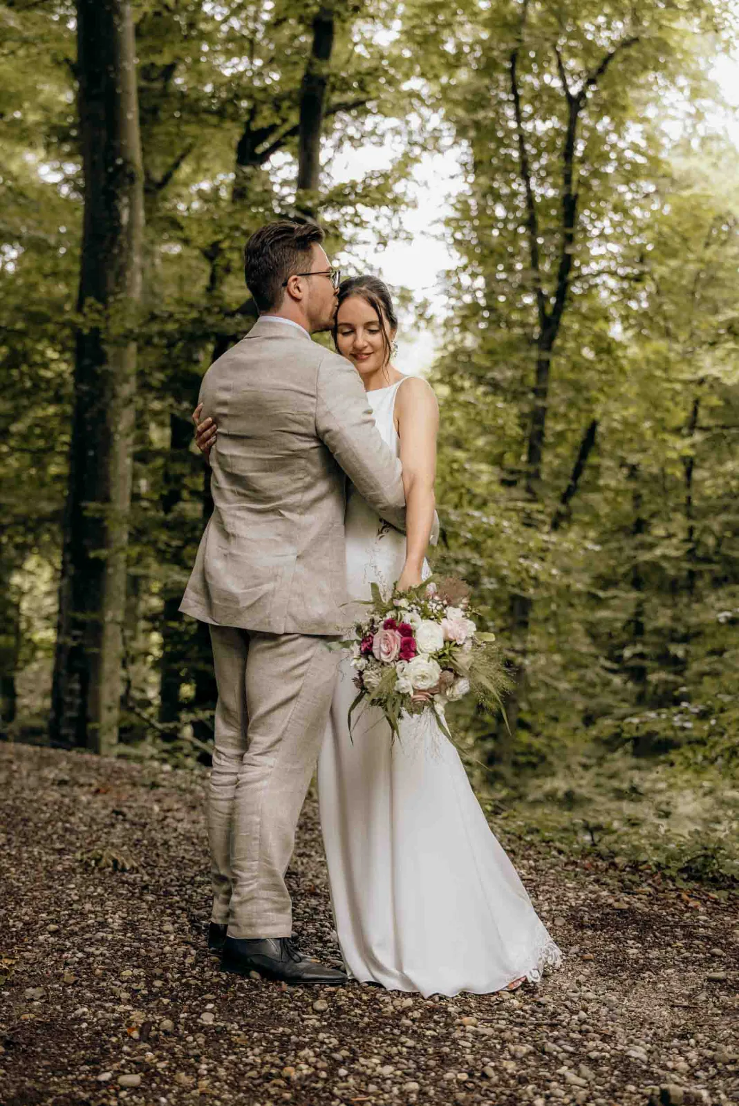 Ein Brautpaar umarmt sich im Wald, während ich als Hochzeitsfotograf München diesen intimen Moment festhalte auf den Weg zur Landgut Kugleralm.